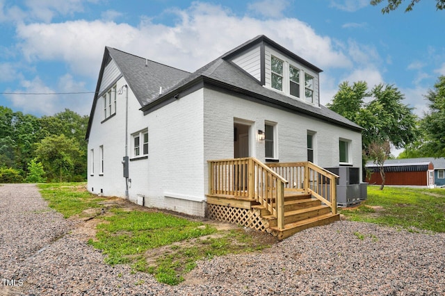 view of front of house featuring a shingled roof, central air condition unit, and brick siding