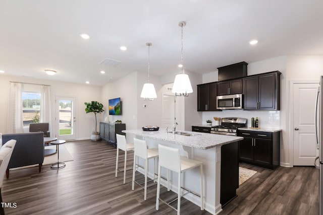 kitchen with stainless steel appliances, a sink, dark wood-style flooring, a center island with sink, and a kitchen breakfast bar