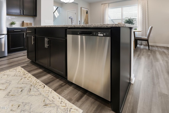 kitchen featuring stainless steel appliances, wood finished floors, light stone countertops, baseboards, and an island with sink