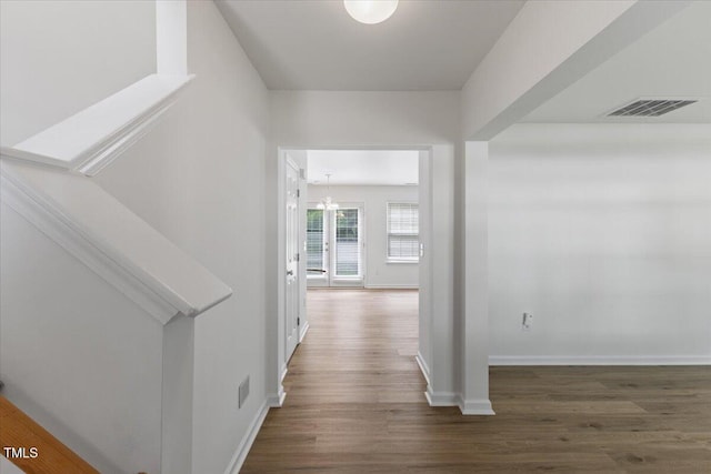 corridor with wood finished floors, a chandelier, and baseboards