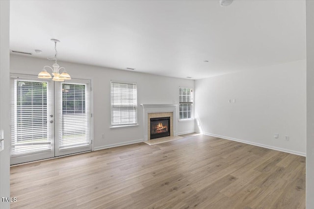 unfurnished living room with french doors, light wood finished floors, baseboards, a chandelier, and a fireplace