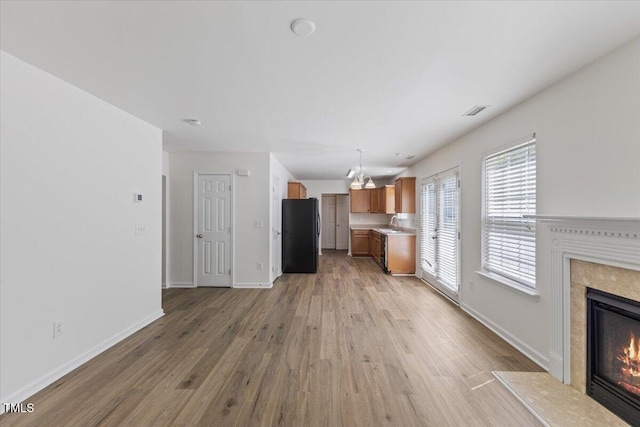 unfurnished living room with a high end fireplace, light wood-type flooring, a chandelier, and baseboards