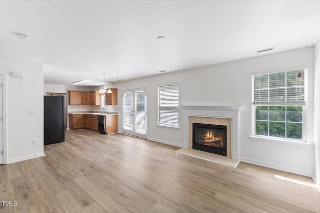 unfurnished living room with baseboards, light wood-style flooring, a high end fireplace, and a chandelier