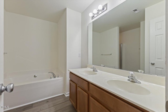 bathroom with wood finished floors, a bath, double vanity, and baseboards