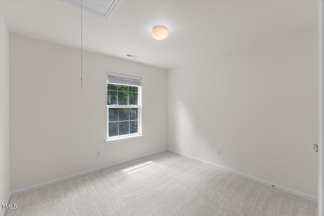 carpeted spare room featuring attic access and baseboards