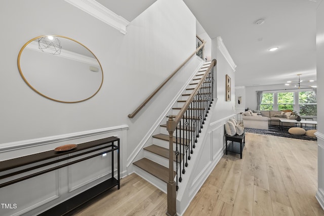 stairs with crown molding, wood finished floors, and a chandelier