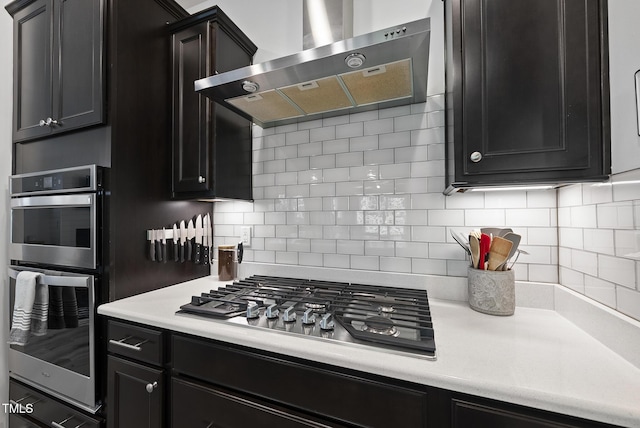 kitchen with exhaust hood, stainless steel appliances, dark cabinetry, and light countertops