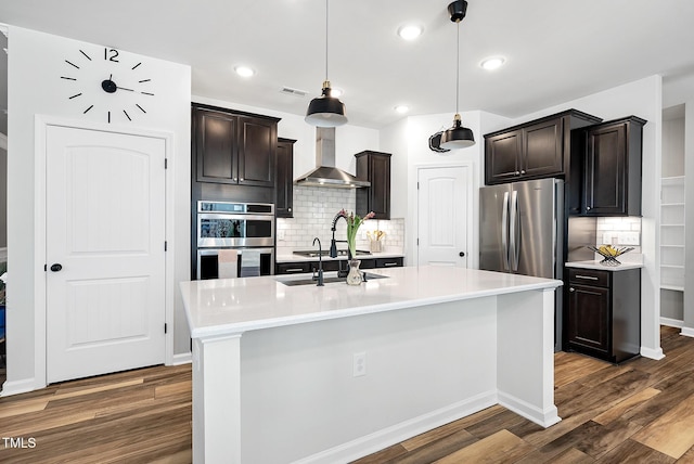 kitchen with wall chimney exhaust hood, stainless steel appliances, decorative backsplash, dark wood-style flooring, and light countertops
