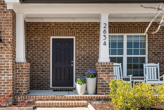 doorway to property with covered porch and brick siding