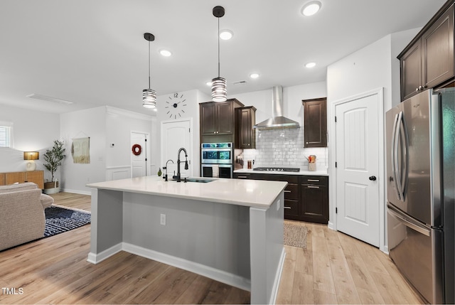 kitchen with appliances with stainless steel finishes, wall chimney range hood, a sink, open floor plan, and dark brown cabinets