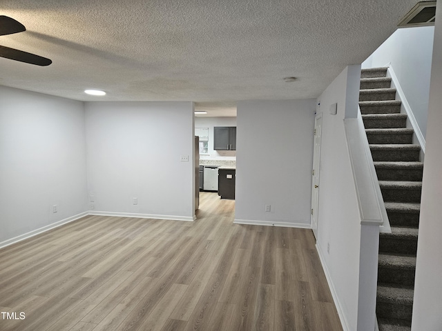 unfurnished living room with light wood finished floors, stairway, a textured ceiling, and ceiling fan