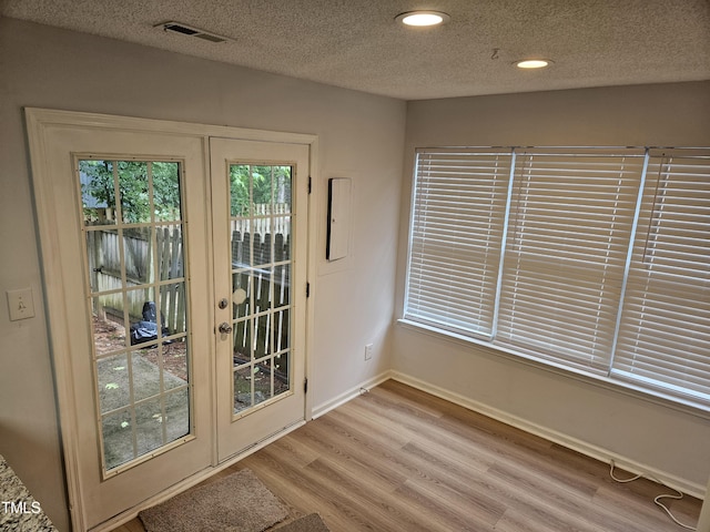 doorway to outside featuring a textured ceiling, wood finished floors, baseboards, recessed lighting, and french doors
