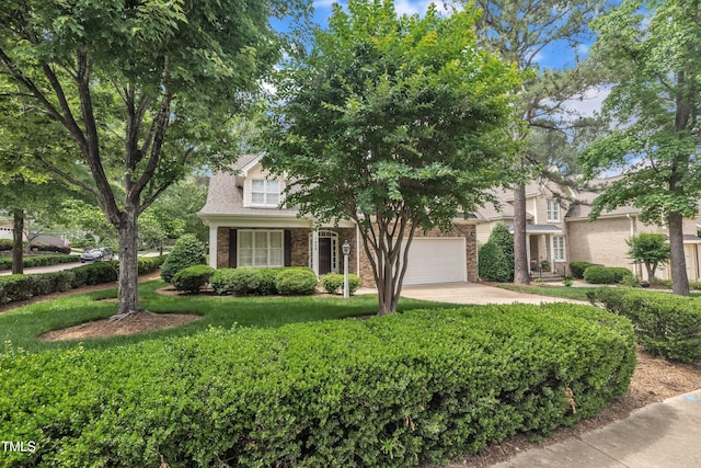 view of property hidden behind natural elements featuring driveway, a front yard, and brick siding