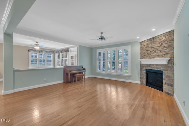 unfurnished living room featuring a ceiling fan, crown molding, wood finished floors, baseboards, and a stone fireplace