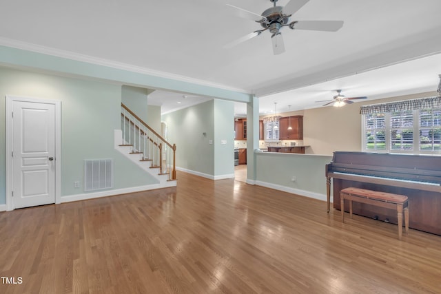 unfurnished living room with ceiling fan, crown molding, stairs, wood finished floors, and baseboards