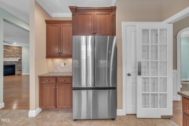 kitchen featuring freestanding refrigerator, light stone countertops, brown cabinets, decorative backsplash, and ornamental molding