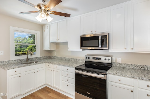 kitchen featuring stainless steel appliances, a sink, white cabinetry, ceiling fan, and light stone countertops