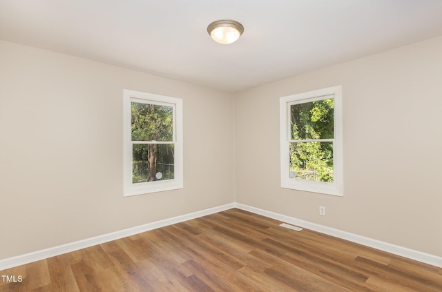 empty room featuring healthy amount of natural light, baseboards, and wood finished floors