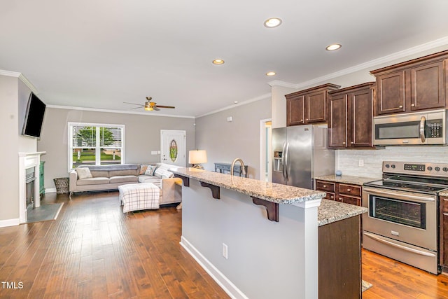 kitchen with stainless steel appliances, a breakfast bar area, a ceiling fan, a fireplace with flush hearth, and decorative backsplash
