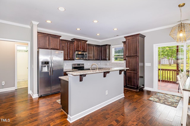kitchen with appliances with stainless steel finishes, a kitchen breakfast bar, decorative backsplash, a kitchen island with sink, and dark wood-style floors