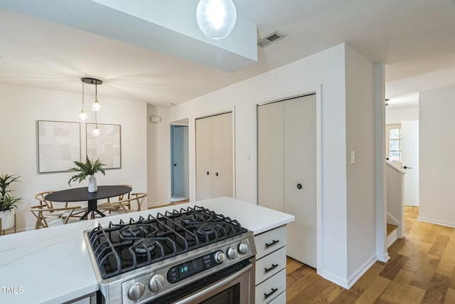kitchen featuring stainless steel range with gas cooktop, light countertops, light wood-style floors, and hanging light fixtures