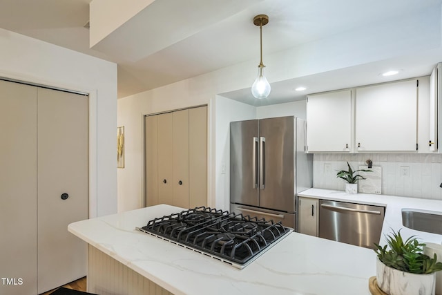 kitchen with stainless steel appliances, white cabinetry, light stone counters, hanging light fixtures, and backsplash