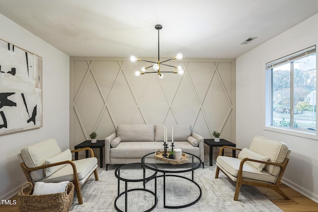 living area featuring a decorative wall, baseboards, a chandelier, and light wood finished floors