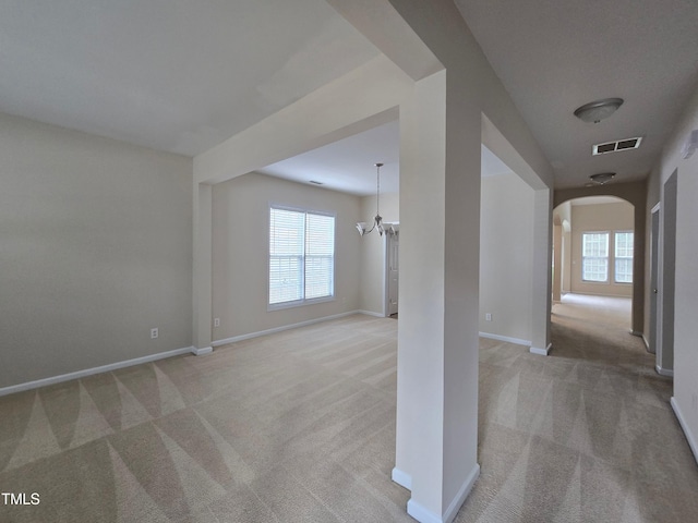 empty room featuring light carpet, arched walkways, and plenty of natural light