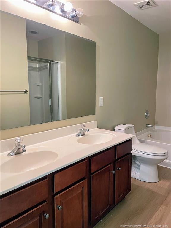 bathroom with a shower, wood finished floors, toilet, and double vanity