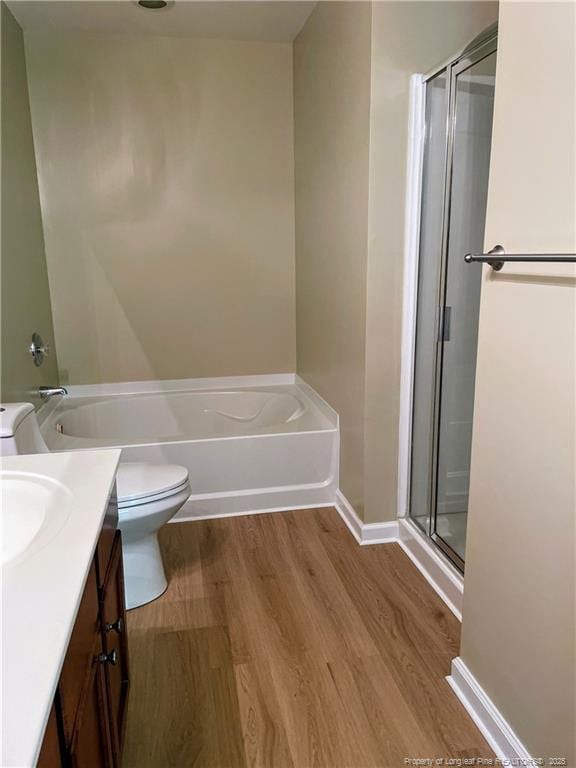full bathroom with wood finished floors, a shower stall, toilet, a bathtub, and vanity