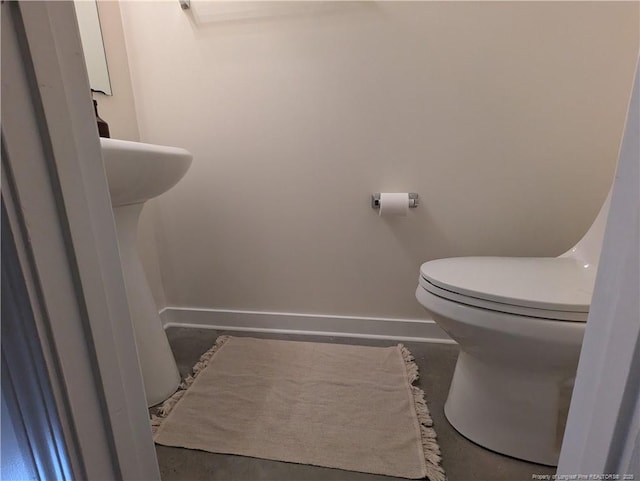 half bath with baseboards, toilet, and concrete floors