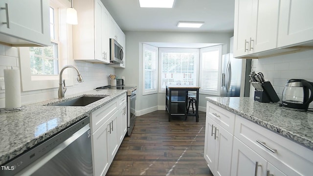 kitchen with appliances with stainless steel finishes, a sink, dark wood-type flooring, white cabinets, and baseboards