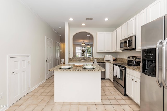 kitchen featuring appliances with stainless steel finishes, white cabinetry, light stone counters, a kitchen island, and ornamental molding