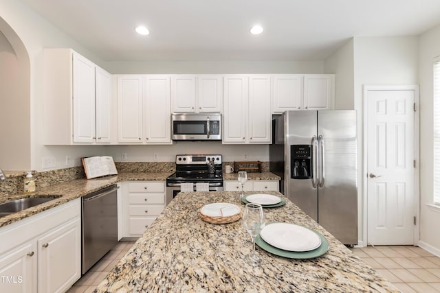 kitchen with appliances with stainless steel finishes, arched walkways, a sink, light tile patterned flooring, and white cabinets