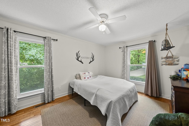 bedroom with wood finished floors, a textured ceiling, crown molding, and a ceiling fan