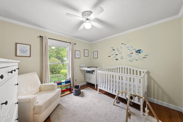 bedroom with crown molding, a nursery area, baseboards, a textured ceiling, and wood finished floors