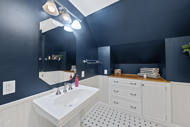 bathroom featuring lofted ceiling, a sink, and a wainscoted wall
