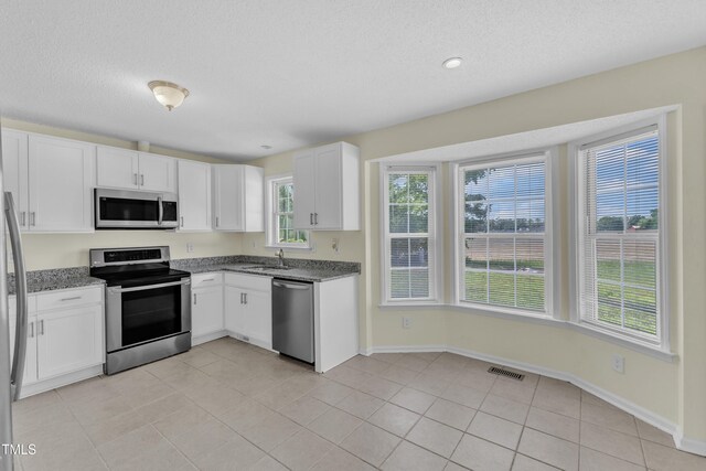 kitchen featuring stainless steel appliances, a sink, white cabinets, healthy amount of natural light, and a textured ceiling