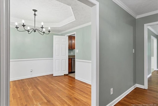 empty room with a textured ceiling, a chandelier, light wood-style flooring, and crown molding