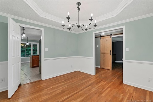 unfurnished room featuring a chandelier, wood finished floors, a barn door, wainscoting, and crown molding