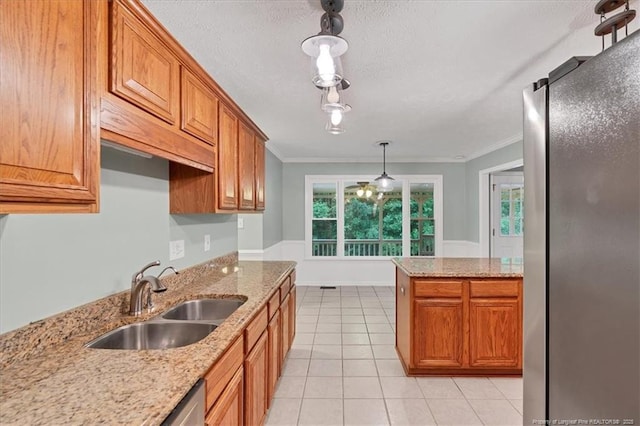 kitchen with a sink, freestanding refrigerator, brown cabinetry, crown molding, and decorative light fixtures