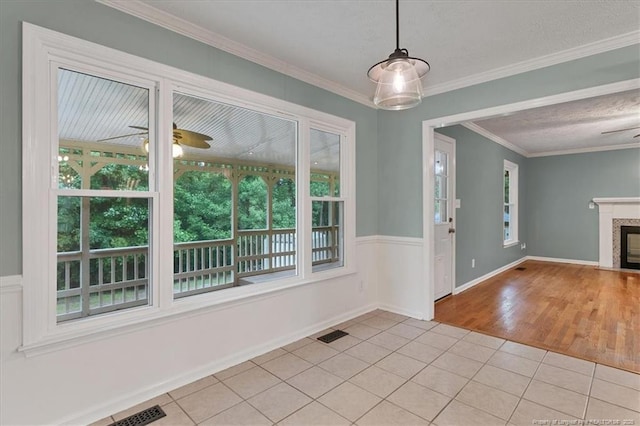 unfurnished dining area with light tile patterned floors, ceiling fan, crown molding, and a fireplace