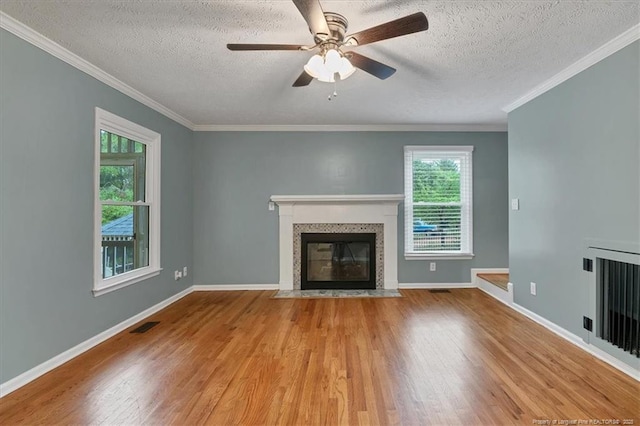 unfurnished living room with a tiled fireplace, wood finished floors, a textured ceiling, crown molding, and baseboards
