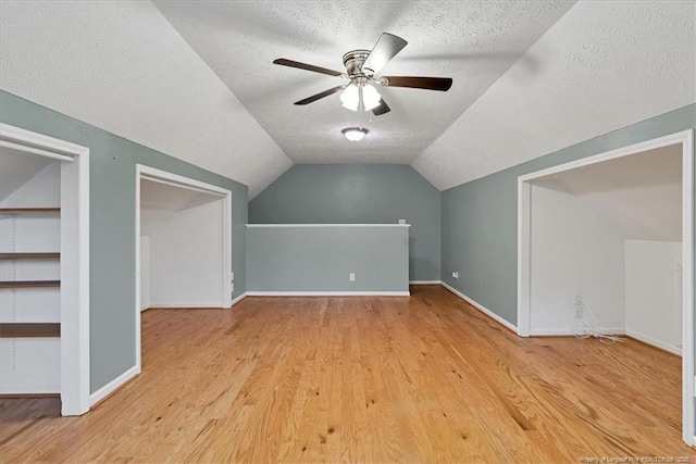 additional living space with a textured ceiling, light wood-type flooring, lofted ceiling, ceiling fan, and baseboards