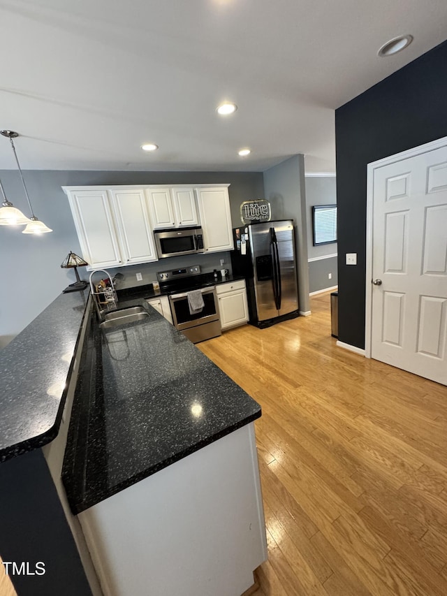 kitchen featuring stainless steel appliances, a sink, white cabinetry, a peninsula, and light wood finished floors