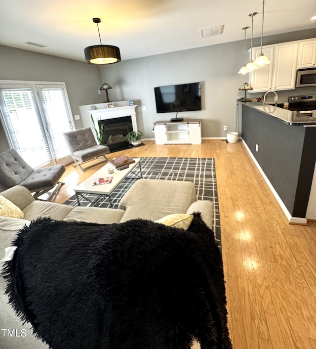 living area with light wood-style flooring, a glass covered fireplace, and baseboards