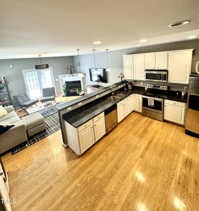 kitchen with stainless steel appliances, a sink, open floor plan, a peninsula, and light wood finished floors