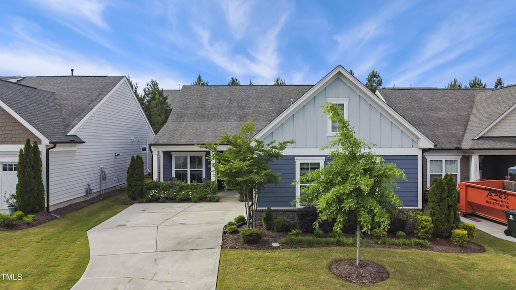 view of front of property with board and batten siding, a front yard, roof with shingles, and concrete driveway