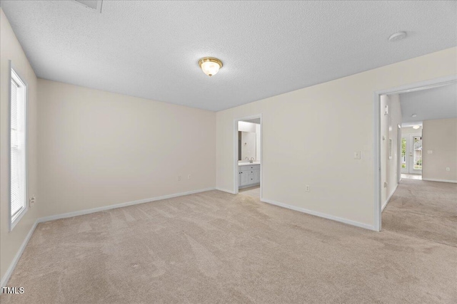 empty room featuring light colored carpet, a textured ceiling, baseboards, and a smoke detector