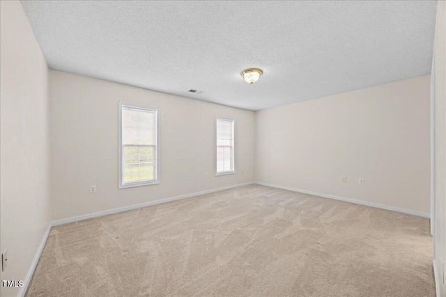 unfurnished room featuring light carpet, a textured ceiling, and baseboards